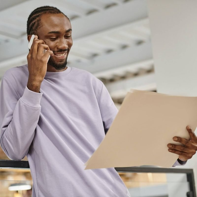 happy-african-american-man-looking-at-project-on-paper-talking-on-smartphone-planning-startup.jpg